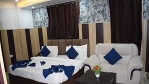 A hotel room with a double bed, a sofa, a small table, and a decorative plant.
