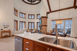 A spacious kitchen with a large island, built-in appliances, and a stone fireplace. - Tremblant Prestige - Manoir 112-10 (Mont-Tremblant)