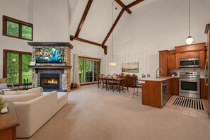 A spacious living room with a fireplace, a television, and a dining area with chairs. - Tremblant Prestige - Manoir 112-10 (Mont-Tremblant)