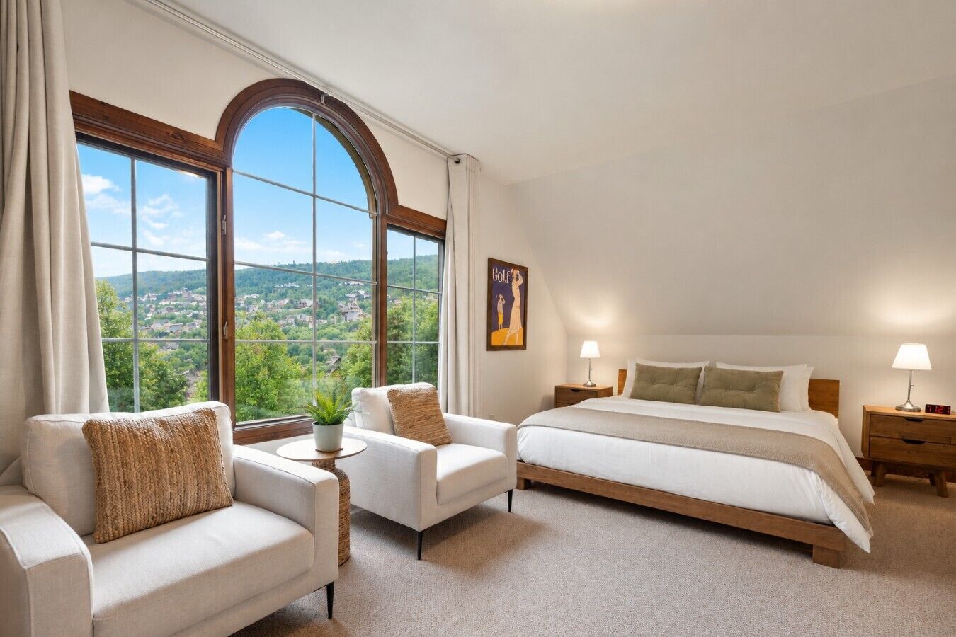 Ein Schlafzimmer mit einem großen Fenster, einem Bett, zwei Sesseln, einem Nachttisch und einer Lampe.