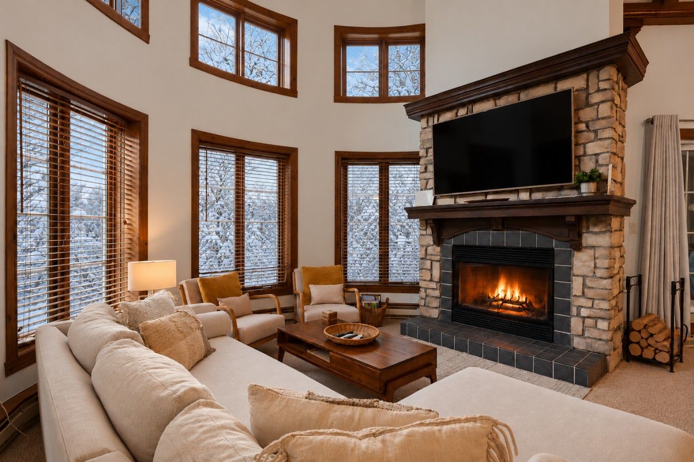 A living room with a stone fireplace, a large flat-screen TV mounted above it, and a cozy seating area with a sofa and armchairs.