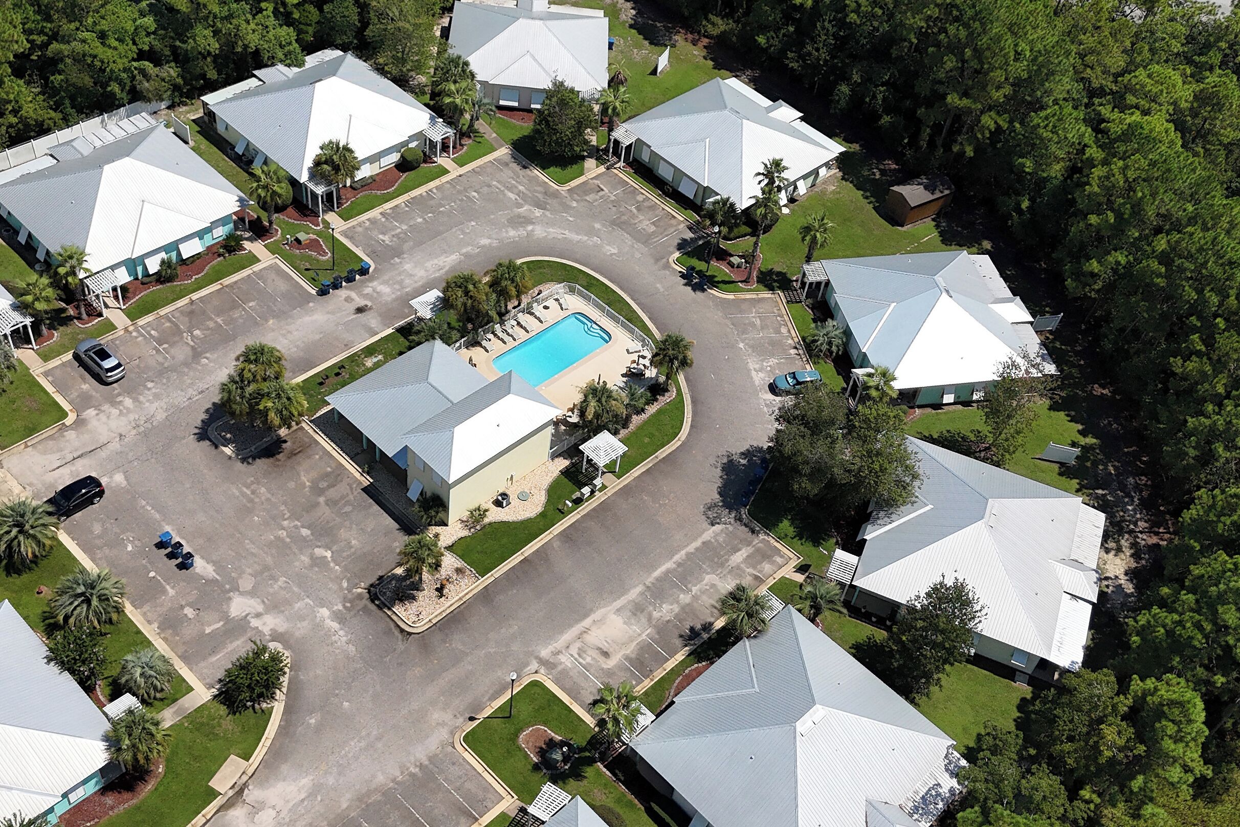 Vue aérienne d’un quartier résidentiel comprenant plusieurs maisons, une piscine et un parking.