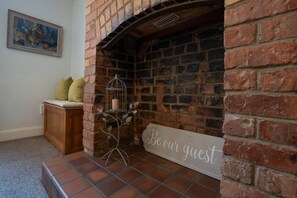 A brick fireplace with a 'Be our guest' sign, a wooden cabinet, and a framed abstract painting on the wall. - Finest Retreats | House on The Green (Derby)