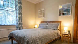 A bedroom with a bed, bedside lamps, a window with curtains, and a small table with a plant. - Finest Retreats | House on The Green (Derby)