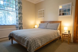 A bedroom with a bed, bedside lamps, a window with curtains, and a small table with a plant. - Finest Retreats | House on The Green (Derby)