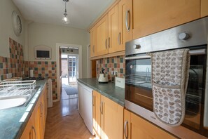 A kitchen with wooden cabinets, a stainless steel oven, and a tiled backsplash. - Finest Retreats | House on The Green (Derby)