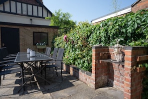 Eine Terrasse im Freien mit Tisch und Stühlen, eine Backsteinmauer und ein Garten mit verschiedenen Pflanzen.