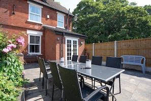 A patio with a table and chairs, a brick house, a wooden fence, and a bench. - Finest Retreats | House on The Green (Derby)