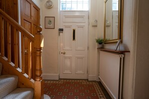 A wooden staircase leading to a white door with a brass handle, a radiator, and a mirror on the wall. - Finest Retreats | House on The Green (Derby)