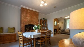 A dining area with a brick fireplace, wooden chairs, a table with a white tablecloth, and a lamp on a wooden side table. - Finest Retreats | House on The Green (Derby)