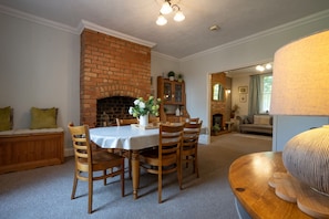 A dining area with a brick fireplace, wooden chairs, a table with a white tablecloth, and a lamp on a wooden side table. - Finest Retreats | House on The Green (Derby)