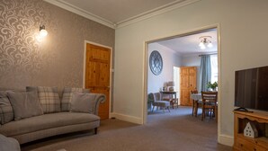 A living room with a sofa, a television, and a dining area with chairs and a table. - Finest Retreats | House on The Green (Derby)