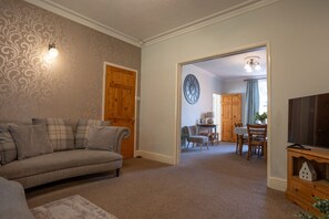 A living room with a sofa, a television, and a dining area with chairs and a table. - Finest Retreats | House on The Green (Derby)