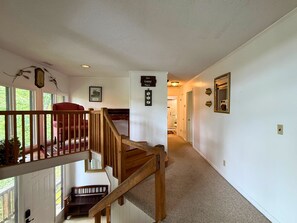 Eine Treppe führt zu einer zweiten Etage, wo ein roter Sessel und eine hölzerne Bank an der Zwischenebene stehen.
