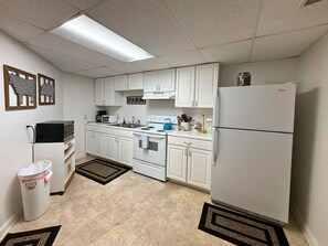 Una cocina con armarios blancos, estufa, fregadero, refrigerador y un bote de basura.
