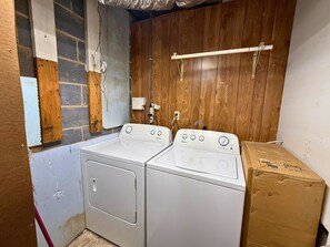 Ein Waschraum mit zwei weißen Waschmaschinen, einer Holzwand und einem Karton.
