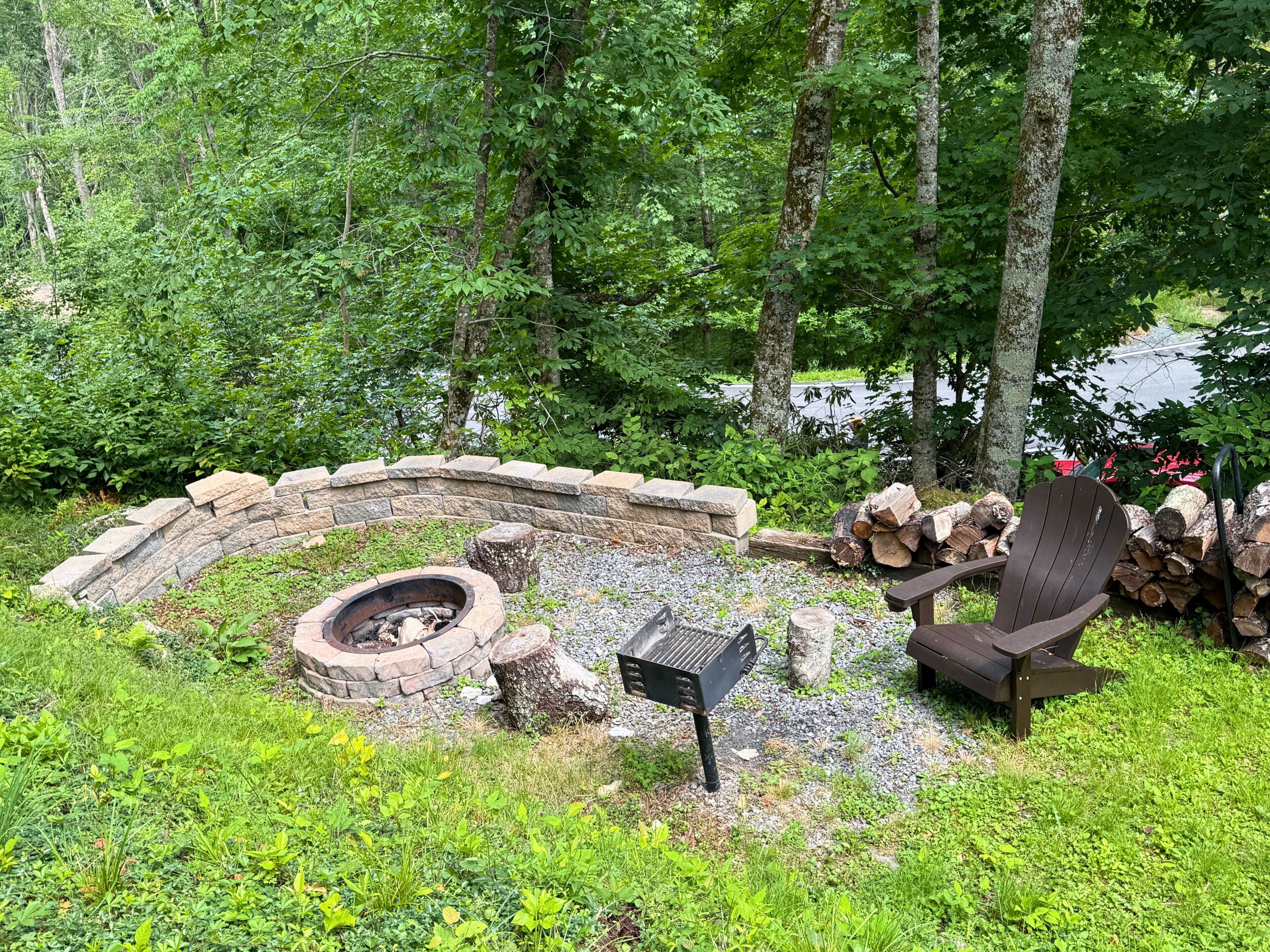 Ein Steinkamin mit einer Steinmauer, ein hölzerner Adirondack-Stuhl und ein Grill.