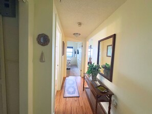 Un couloir avec un plancher en bois, un tapis, un banc et un miroir accroché au mur.