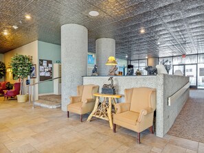 Eine Lobby mit hoher Decke, einem Empfangstresen, zwei Sesseln, einem kleinen Tisch und einer Zimmerpflanze.