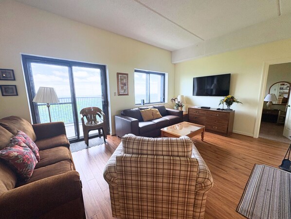 Een woonkamer met een bank, een fauteuil, een salontafel, een televisie en een balkon met uitzicht.