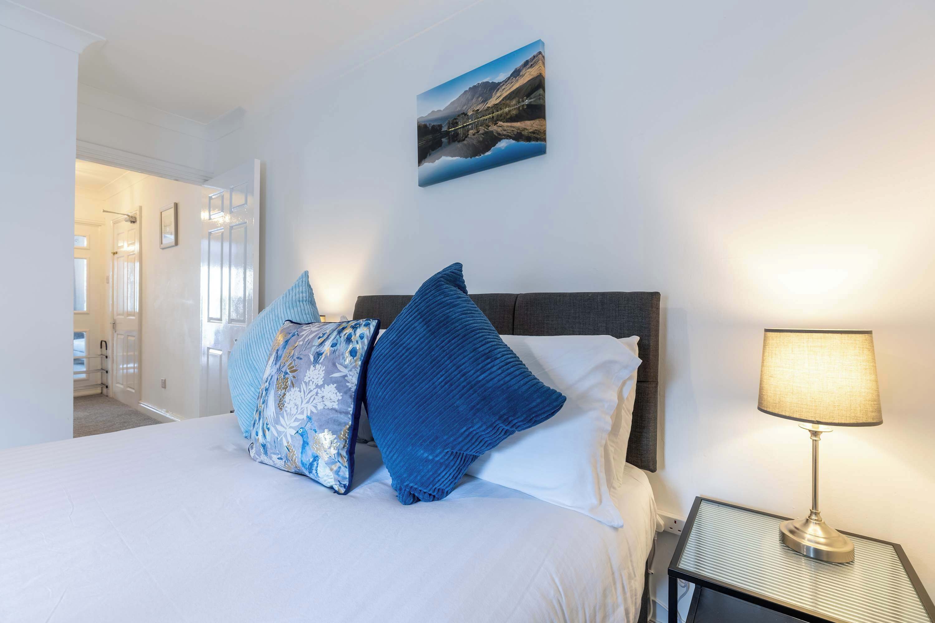 A neatly made bed with two pillows, a bedside lamp, and a framed picture on the wall.