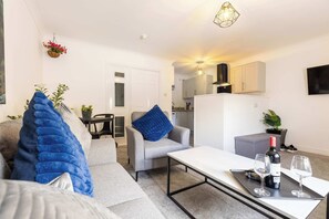 Ein Wohnzimmer mit einer Couch, einem Sessel, einem Couchtisch und einer Ablage mit Flasche und Gläsern.