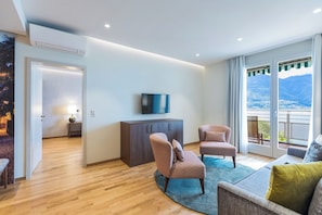 A modern living room with a flat-screen TV, two patterned armchairs, a sofa, and a large window with a view of mountains. - Casa Palma (Muralto)
