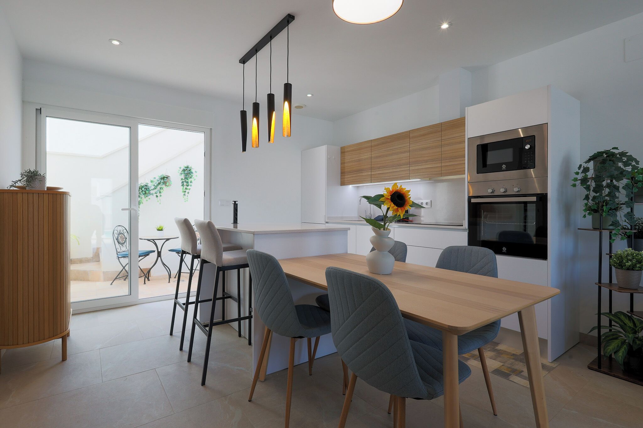 Een moderne keuken met een inbouwoven, een magnetron en een eethoek met een houten tafel en grijze stoelen.
