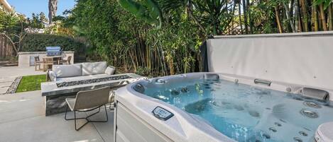 A hot tub with a control panel, a seating area with a sofa and chairs, and a grill.