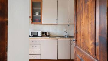 Een keuken met kastjes, een magnetron, een waterkoker en een spoelbak.