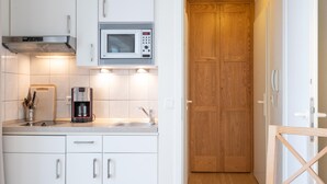 A kitchen with white cabinets, a microwave, a coffee maker, and a wooden door. - Stylische Ferienwohnung fur Zwei mit Balkon im Seepark Sellin (Sellin)