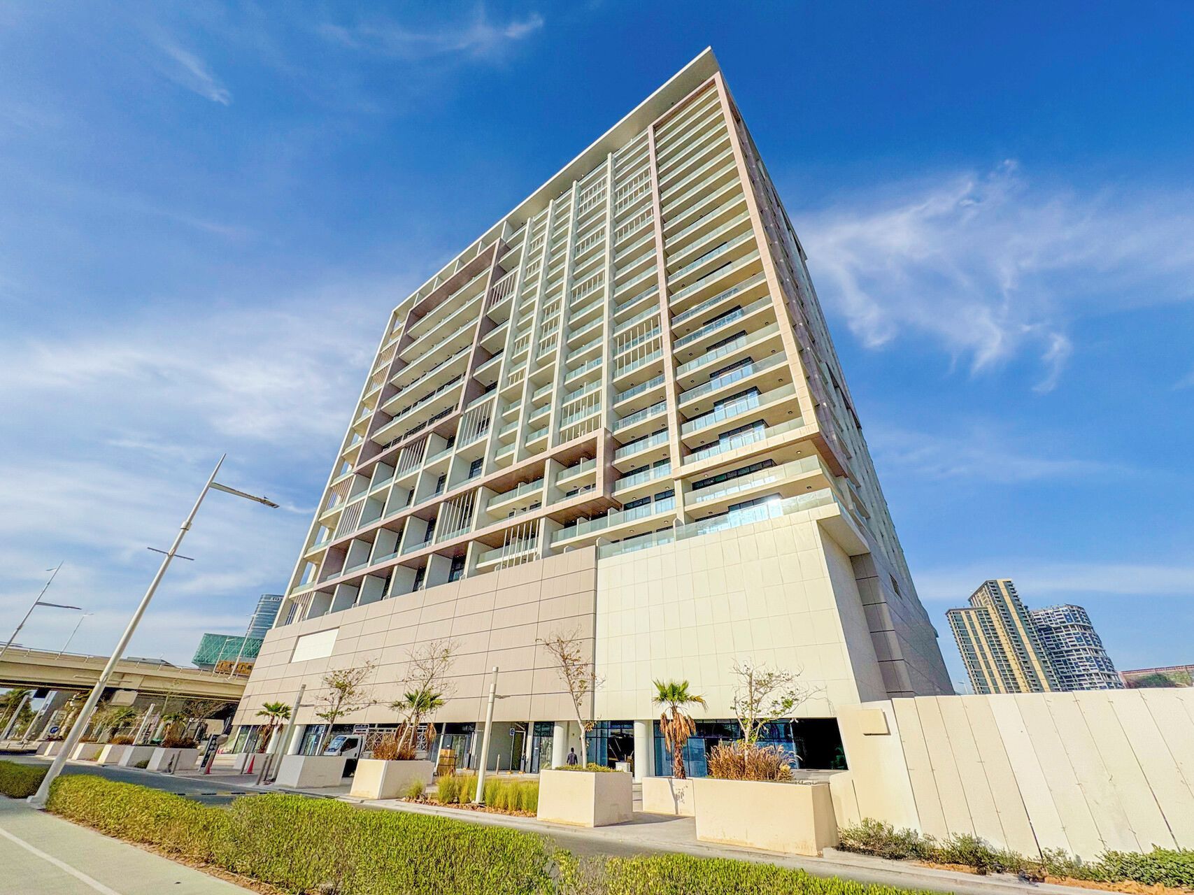 A modern high-rise building with multiple balconies, a flat roof, and a clear sky.