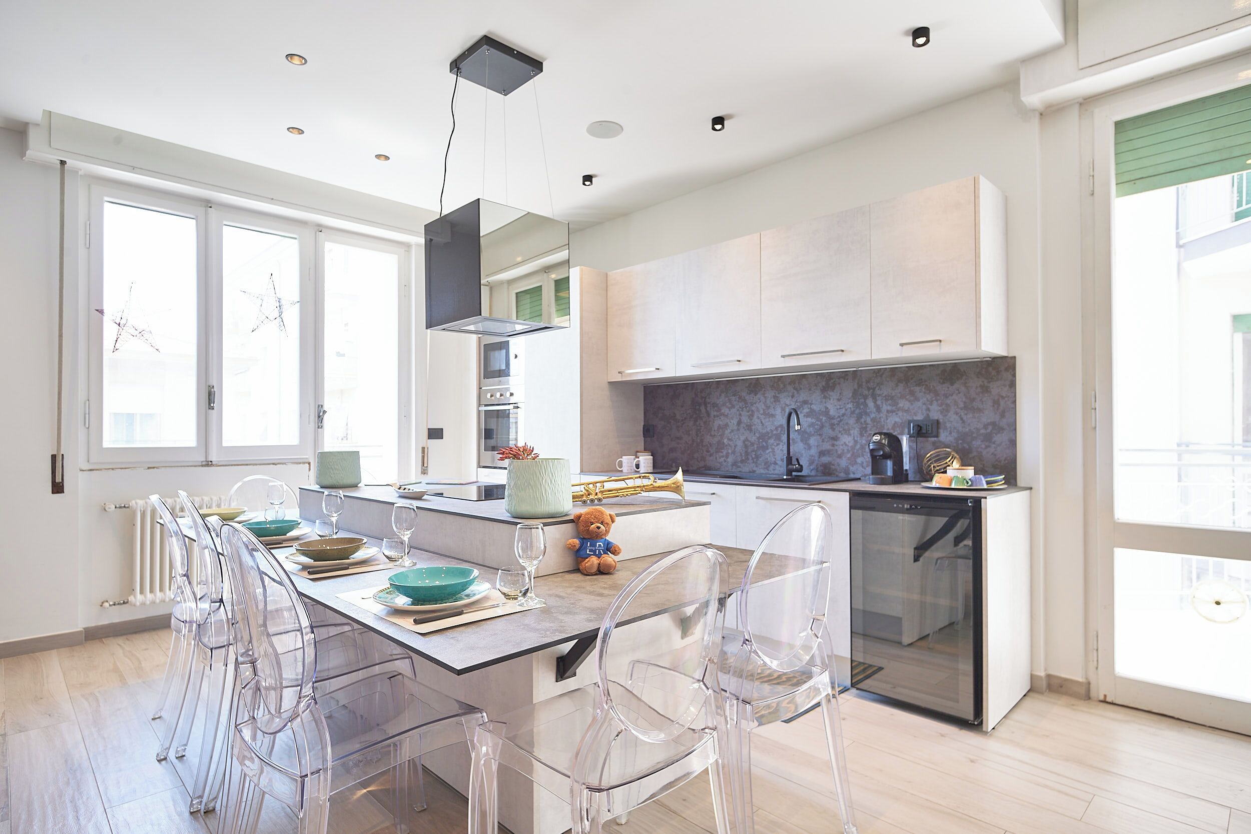 A modern kitchen with a central island, clear chairs, and a dining table.