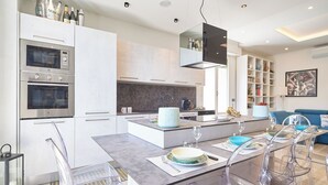 Una cucina moderna con elettrodomestici integrati, un'isola centrale con posti a sedere e un'area pranzo con sedie trasparenti.