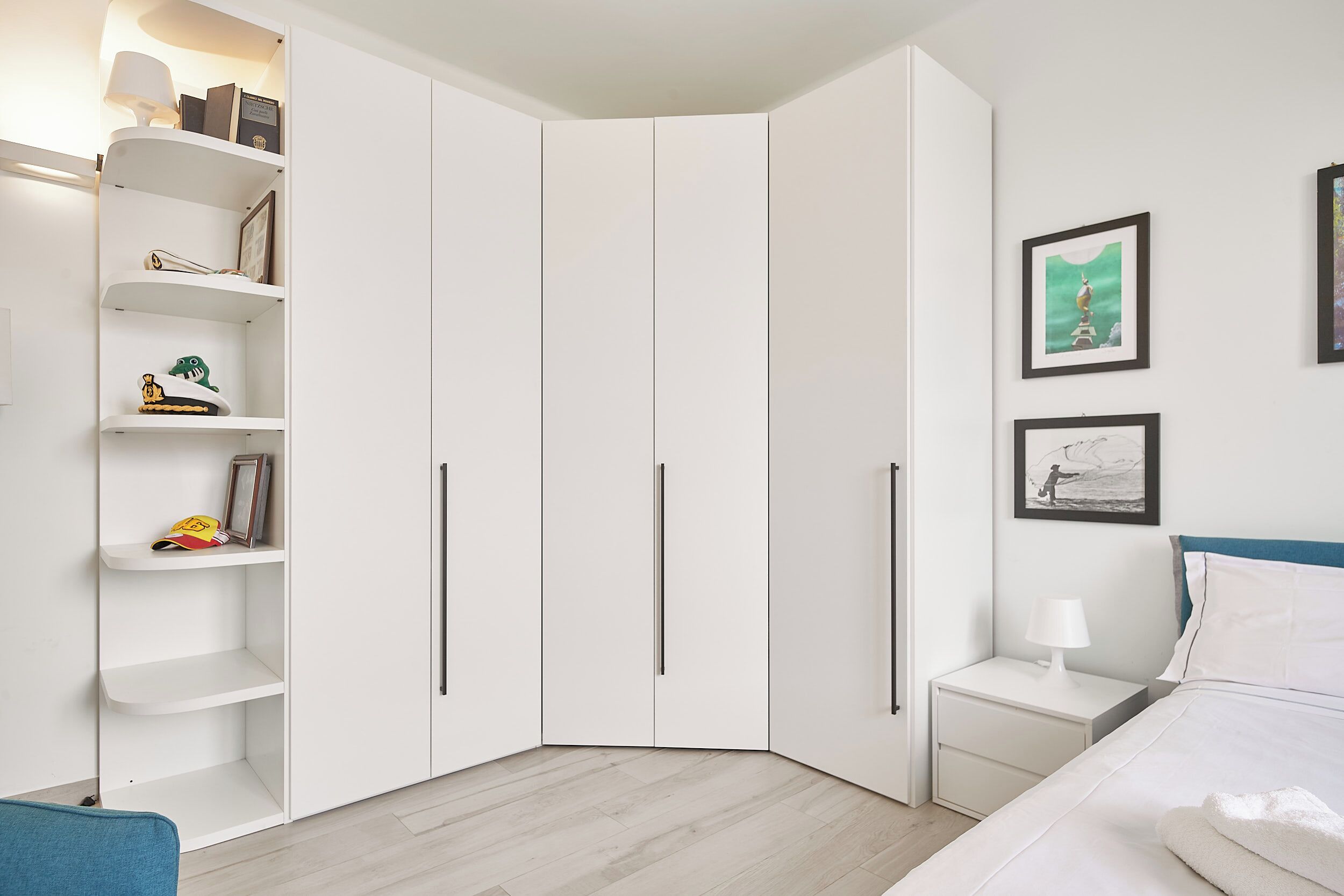 Een slaapkamer met een bed, nachtkastje, witte kledingkast en plank met diverse spullen.