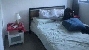 Ein Einzelbett mit weißer Bettwäsche, ein Nachttisch mit Lampe und ein Fenster mit Vorhängen.