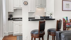 A kitchen with white cabinets, a black countertop, and a wooden chair. - Walk to Forsyth Park, Dining & Savannah Squares by Lucky Savannah (Savannah)