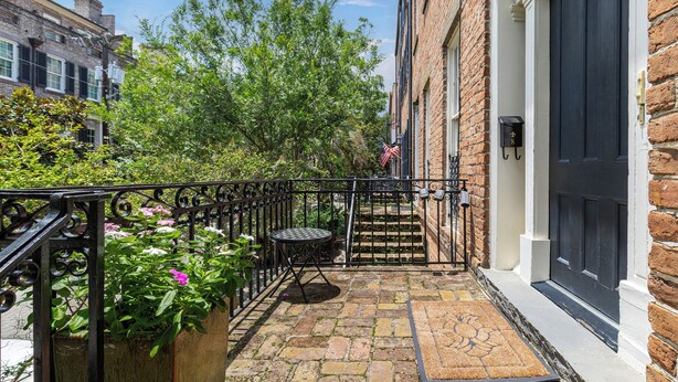 A brick building with a black door, a small outdoor seating area with a table and chairs, and a mailbox. - Walk to Forsyth Park, Dining & Savannah Squares by Lucky Savannah (Savannah)