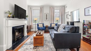 A living room with a fireplace, a sofa, a coffee table, and a television. - Walk to Forsyth Park, Dining & Savannah Squares by Lucky Savannah (Savannah)