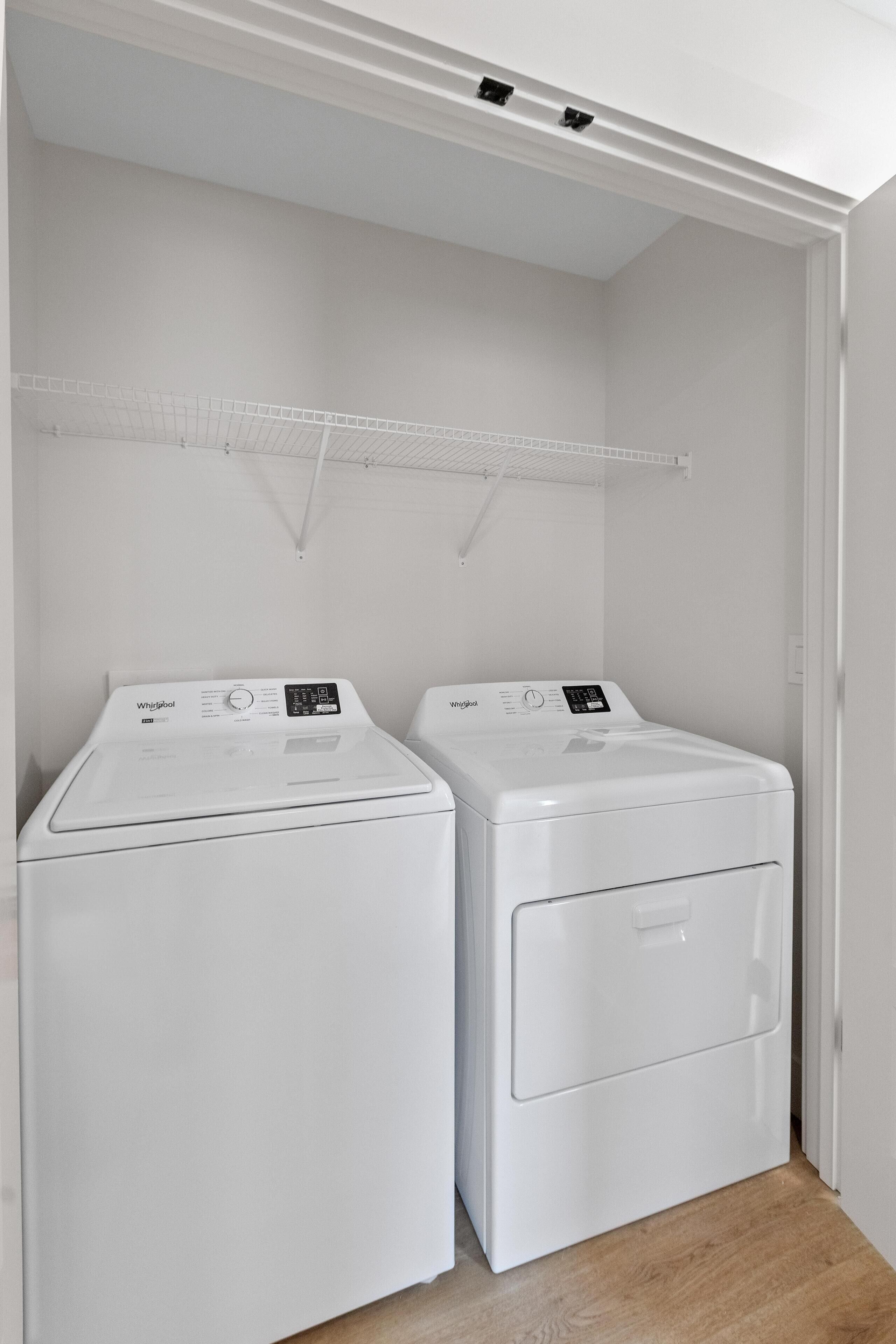 Une buanderie équipée de deux machines à laver et de deux sèche-linge Whirlpool blancs, avec un plafond blanc et un plancher en bois.