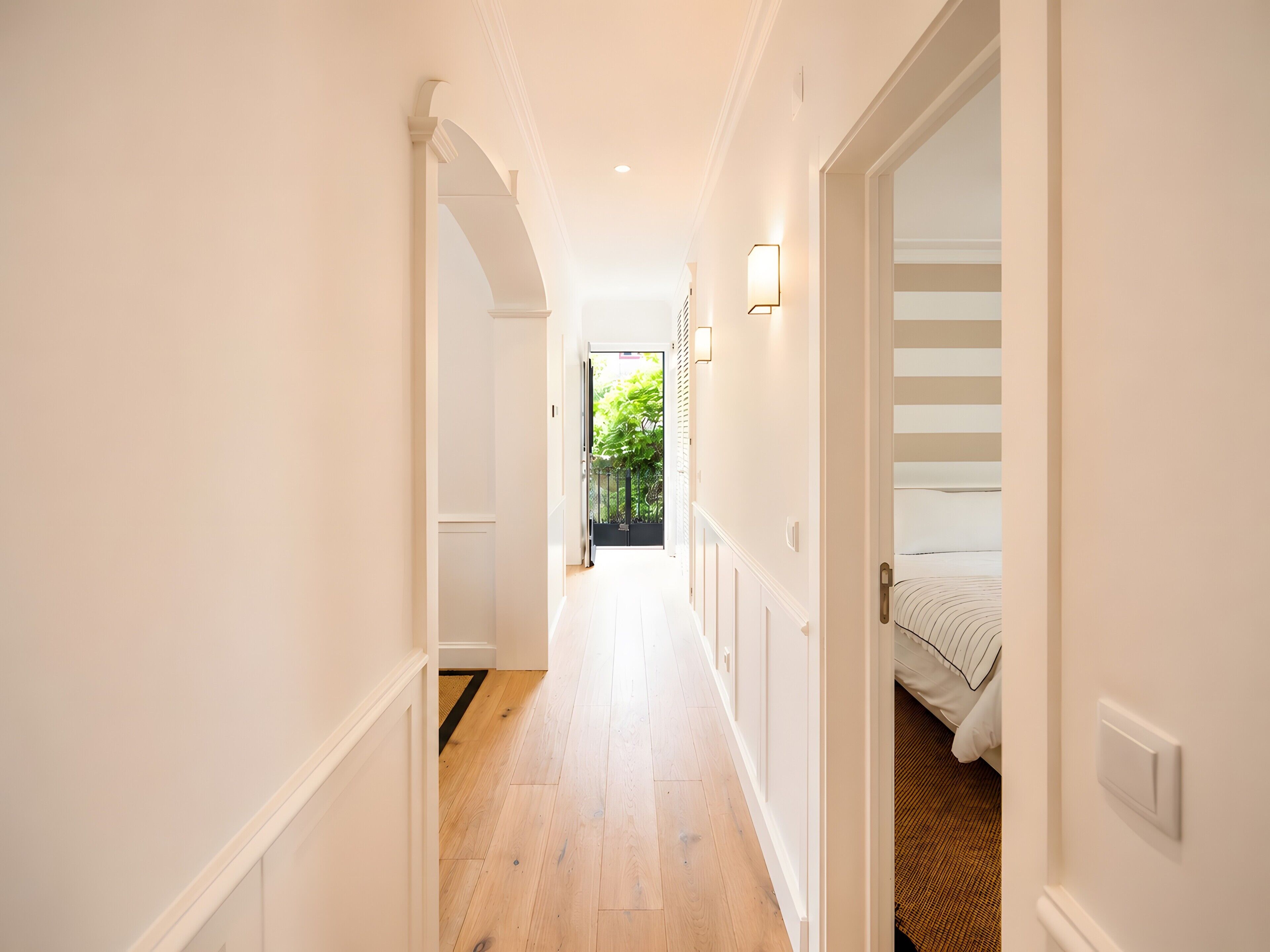 Een gang met houten vloer, witte muren en een bed met gestreept beddengoed aan het einde van de kamer.