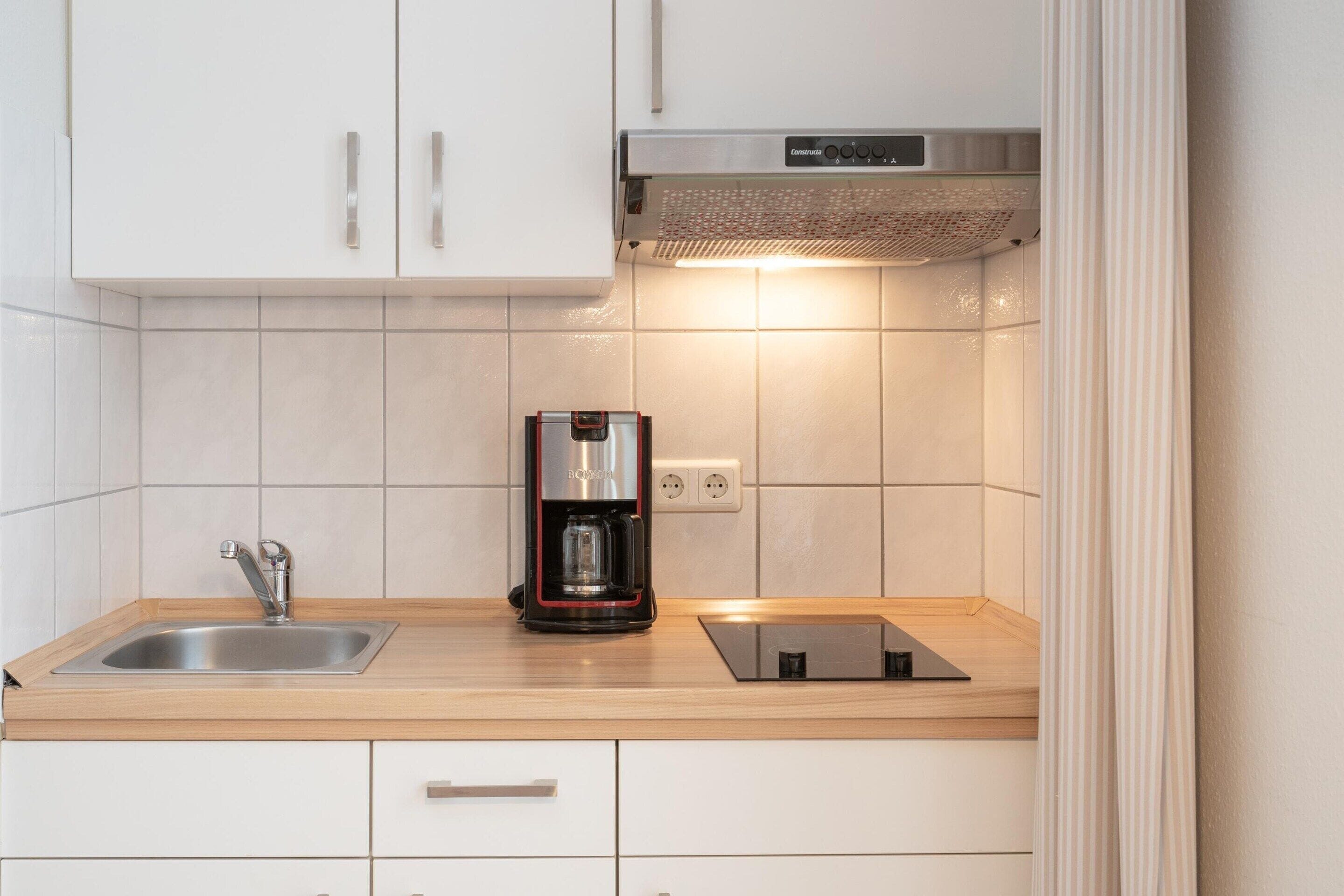A kitchen with a stainless steel sink, a coffee maker, a built-in oven, and white cabinets.
