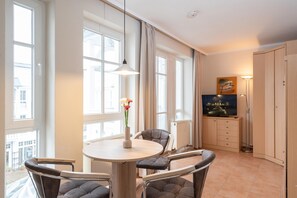 A modern room with a dining table, chairs, a vase with flowers, a television, and a cabinet. - Gemutliche Ferienwohnung im Ostseebad Sellin mit Balkon (Sellin)