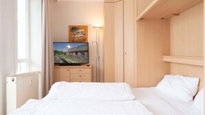 A hotel room with a bed, a TV on a stand, a radiator, a wardrobe, and a painting on the wall. - Gemutliche Ferienwohnung im Ostseebad Sellin mit Balkon (Sellin)