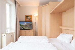 A hotel room with a bed, a TV on a stand, a radiator, a wardrobe, and a painting on the wall. - Gemutliche Ferienwohnung im Ostseebad Sellin mit Balkon (Sellin)