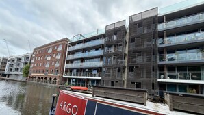 Ein modernes Gebäude mit mehreren Balkonen und einem Boot namens 'ARGO', das an einem Kanal vor Anker liegt.