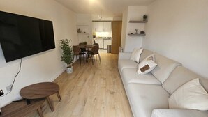 Ein Wohnzimmer mit Sofa, Fernseher, Esstisch, Stühlen und einer Zimmerpflanze.