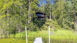 A wooden deck leading to a cabin surrounded by dense forest and a pond with lily pads. - Private Sampson Lake frontage home - Bordering Whitefish City Limits (Whitefish)
