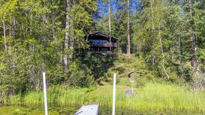 A cabin surrounded by trees, a dock extending into a pond with lily pads, and a clear sky. - Private Sampson Lake frontage home - Bordering Whitefish City Limits (Whitefish)