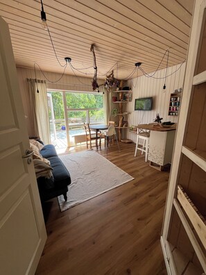 A cozy cabin interior with a wooden floor, a dining area, a sofa, and a TV mounted on the wall. - Vacation at an Organic Farm (Schashagen)